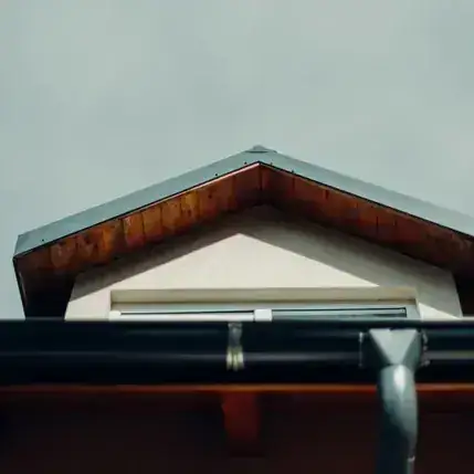 Dark steel gutter and downspout against a cloudy sky